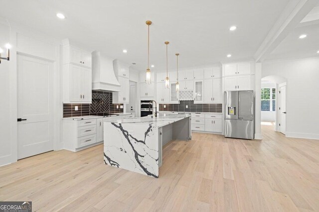 1387 Mineral Springs Rd, Hoschton, GA 30548 - kitchen with stainless steel appliances, premium range hood, arched walkways, tasteful backsplash, and light wood-style floors
