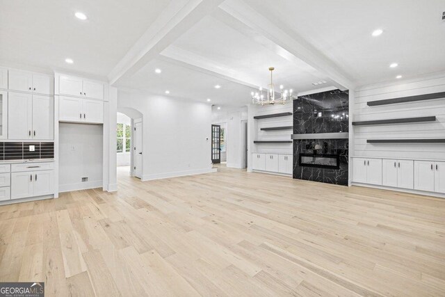 1387 Mineral Springs Rd, Hoschton, GA 30548 - unfurnished living room with arched walkways, light wood-style floors, beam ceiling, a chandelier, and a premium fireplace