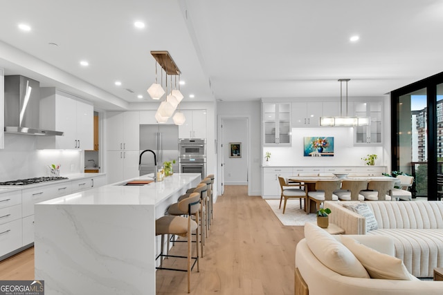 2425 Peachtree Rd NE Unit 902, Atlanta, GA 30305 - kitchen with wall chimney exhaust hood, appliances with stainless steel finishes, light wood-type flooring, a kitchen breakfast bar, and glass insert cabinets