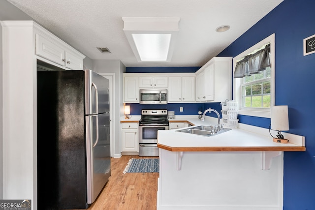 135 Pinewood Cir, Colbert, GA 30628 - kitchen with stainless steel appliances, a peninsula, light wood-style floors, white cabinets, and a kitchen breakfast bar
