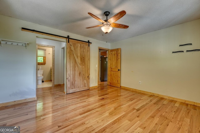 224 Shake Rag Rd, Hiawassee, GA 30546 - unfurnished bedroom featuring light wood finished floors, a barn door, baseboards, a textured ceiling, and ensuite bathroom