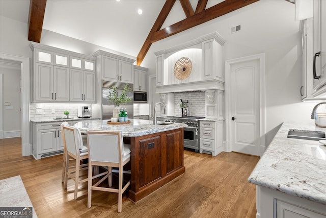 3057 Watsons Bnd, Milton, GA 30004 - kitchen featuring built in appliances, backsplash, high vaulted ceiling, a center island with sink, and light stone counters