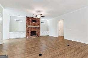 5924 Mitchell St, Flowery Branch, GA 30542 - unfurnished living room featuring a ceiling fan, wood finished floors, a brick fireplace, and crown molding