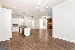 5924 Mitchell St, Flowery Branch, GA 30542 - kitchen with open floor plan, dark wood finished floors, a chandelier, a center island with sink, and crown molding