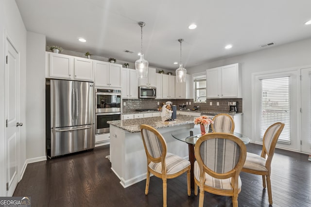 3755 Gardenside Ct, Alpharetta, GA 30004 - kitchen featuring appliances with stainless steel finishes, a center island, decorative backsplash, white cabinetry, and light stone countertops
