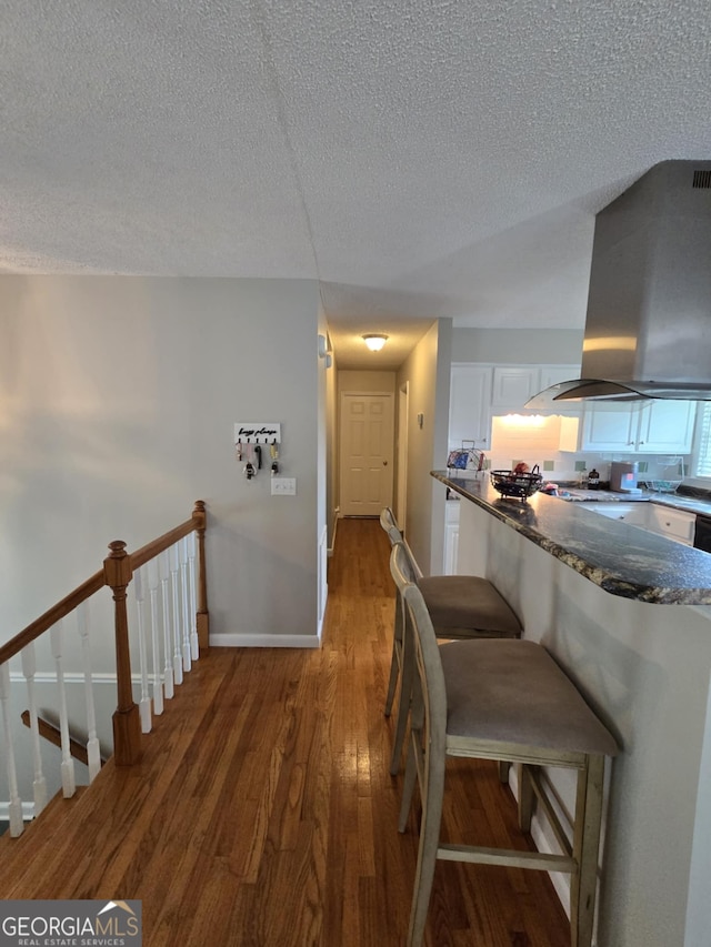 1214 Tucker Rd, Perry, GA 31069 - kitchen with island range hood, white cabinets, wood finished floors, a textured ceiling, and baseboards