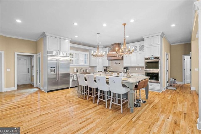 4670 Hamden Forest Dr SW, Atlanta, GA 30331 - kitchen featuring appliances with stainless steel finishes, a chandelier, ornamental molding, premium range hood, and a breakfast bar area