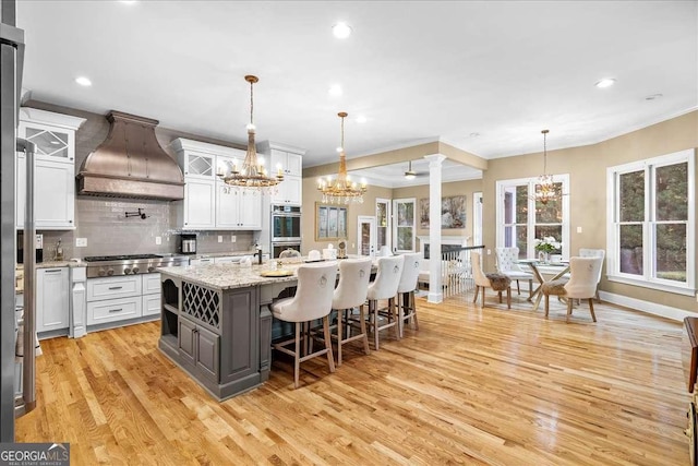 4670 Hamden Forest Dr SW, Atlanta, GA 30331 - kitchen with custom exhaust hood, a chandelier, light wood finished floors, white cabinetry, and crown molding
