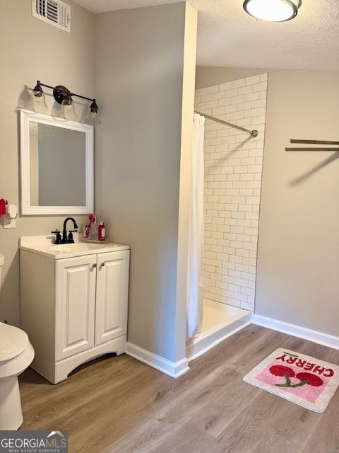 219 Broad St, Carrollton, GA 30117 - full bath featuring toilet, wood finished floors, a tile shower, vanity, and baseboards