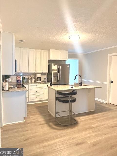 219 Broad St, Carrollton, GA 30117 - kitchen featuring stainless steel fridge with ice dispenser, white cabinets, light wood-style floors, a kitchen island with sink, and a kitchen breakfast bar