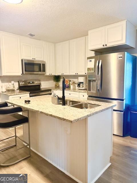 219 Broad St, Carrollton, GA 30117 - kitchen with appliances with stainless steel finishes, light wood-type flooring, white cabinetry, light stone countertops, and a textured ceiling