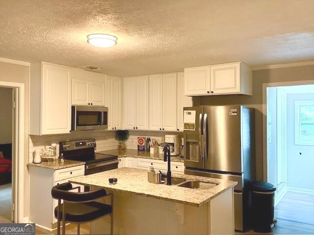 219 Broad St, Carrollton, GA 30117 - kitchen with appliances with stainless steel finishes, white cabinetry, light stone countertops, a sink, and crown molding