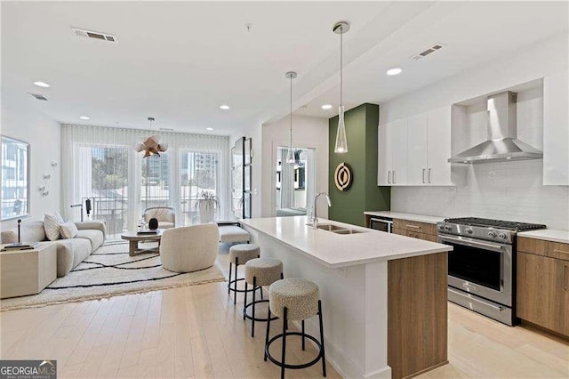 775 Juniper St NE Unit 111, Atlanta, GA 30308 - kitchen with wall chimney range hood, stainless steel range with gas stovetop, a breakfast bar area, open floor plan, and an island with sink
