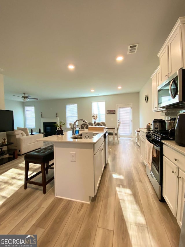 2757 Malton Way, Loganville, GA 30052 - kitchen with appliances with stainless steel finishes, white cabinetry, light wood-style flooring, a kitchen island with sink, and healthy amount of natural light