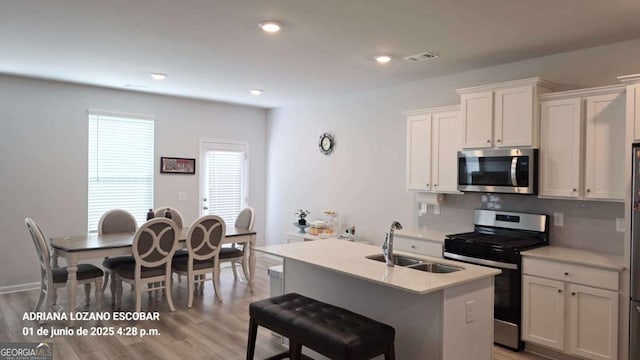 2757 Malton Way, Loganville, GA 30052 - kitchen featuring appliances with stainless steel finishes, light countertops, white cabinets, light wood-style flooring, and an island with sink