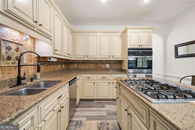 1039 Avery Creek Dr, Woodstock, GA 30188 - kitchen featuring appliances with stainless steel finishes, cream cabinetry, arched walkways, tasteful backsplash, and light wood-style flooring
