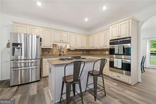 1039 Avery Creek Dr, Woodstock, GA 30188 - kitchen with appliances with stainless steel finishes, cream cabinetry, arched walkways, crown molding, and decorative backsplash
