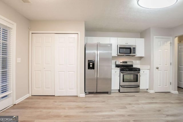 7113 Ambercrest Ct, Austell, GA 30168 - kitchen featuring appliances with stainless steel finishes, white cabinetry, light wood-type flooring, and a textured ceiling
