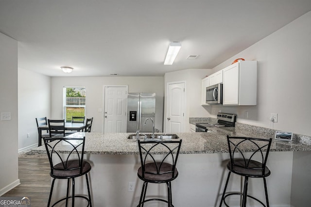 1776 Cheryl Ave, Griffin, GA 30224 - kitchen with appliances with stainless steel finishes, a peninsula, dark wood finished floors, light stone countertops, and white cabinetry