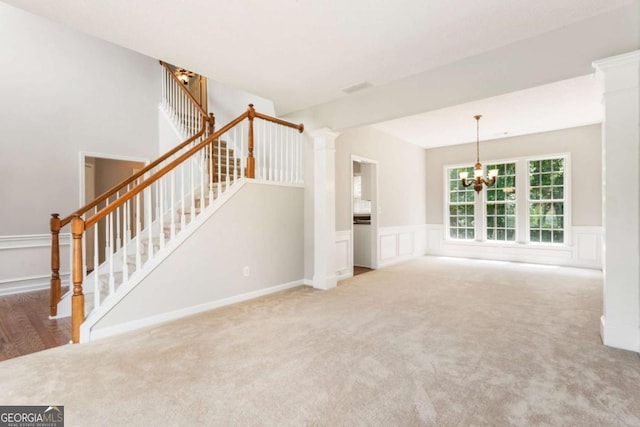 144 Nocatee Trl, Woodstock, GA 30188 - unfurnished living room with carpet flooring, a chandelier, stairs, a wainscoted wall, and ornate columns