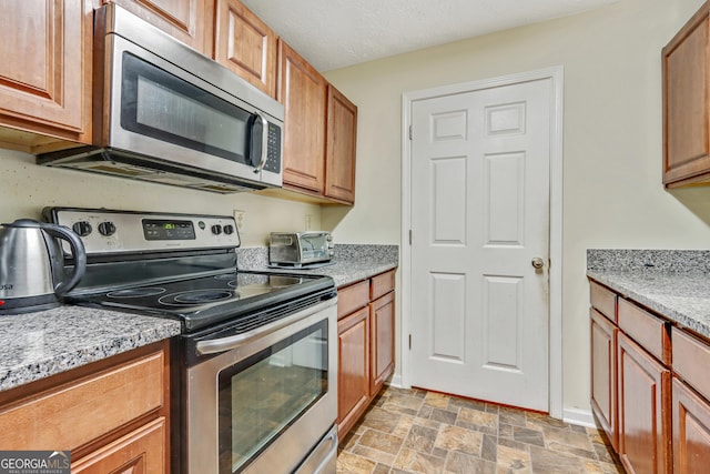 12303 Waldrop Pl, Decatur, GA 30034 - kitchen featuring appliances with stainless steel finishes, stone finish flooring, brown cabinets, and light stone countertops