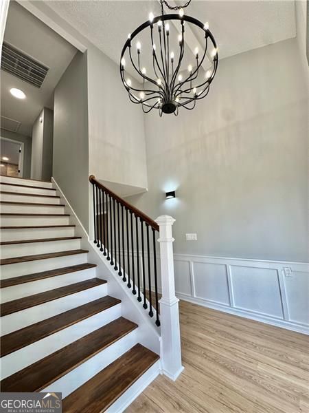 5419 Lake Dr, Douglasville, GA 30135 - stairway with a chandelier, wood finished floors, a wainscoted wall, and a decorative wall