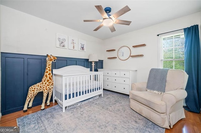 4458 Trickum Rd, Marietta, GA 30066 - bedroom featuring wood finished floors, a nursery area, ceiling fan, and a wainscoted wall