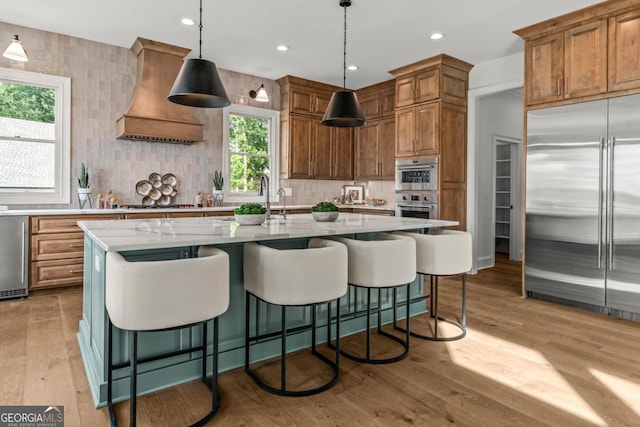 117 W View Way, Eatonton, GA 31024 - kitchen featuring appliances with stainless steel finishes, premium range hood, tasteful backsplash, light wood finished floors, and brown cabinetry