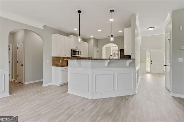 766 Chapman St, Jonesboro, GA 30238 - kitchen featuring stainless steel microwave, a kitchen breakfast bar, light wood-style flooring, dark stone countertops, and white cabinets