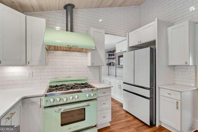 14905 Thompson Rd, Milton, GA 30004 - kitchen featuring freestanding refrigerator, gas stove, wall chimney exhaust hood, decorative backsplash, and white cabinetry