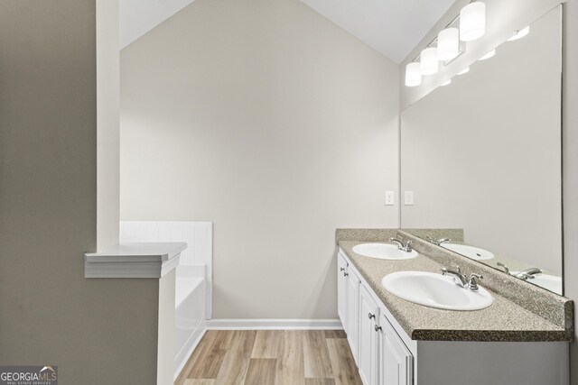 165 Heaton Place Trl, Covington, GA 30016 - bathroom featuring vaulted ceiling, wood finished floors, double vanity, a bath, and baseboards
