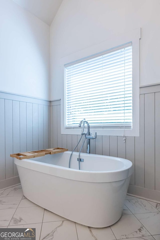 1753 Russell St SE, Atlanta, GA 30316 - bathroom featuring marble look tile flooring, wainscoting, healthy amount of natural light, a freestanding tub, and vaulted ceiling