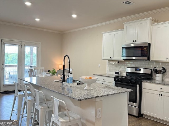 5996 Screech Owl Dr, Flowery Branch, GA 30542 - kitchen with appliances with stainless steel finishes, crown molding, an island with sink, white cabinetry, and light stone countertops