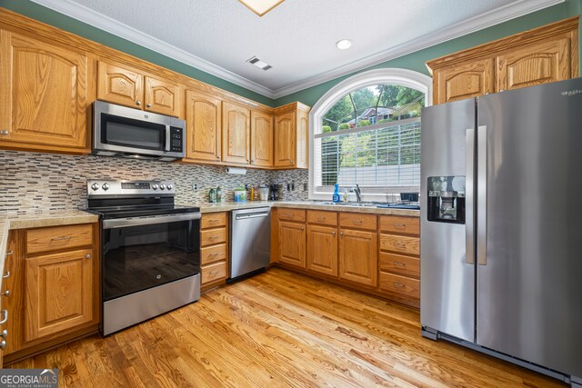 894 Oak Pointe Dr, Cleveland, GA 30528 - kitchen with appliances with stainless steel finishes, crown molding, light wood finished floors, a sink, and tasteful backsplash