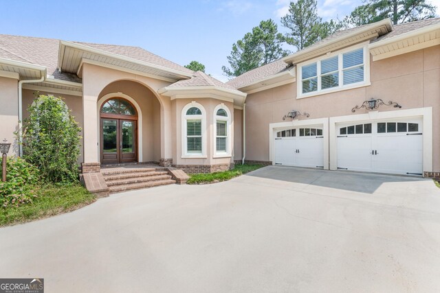 353 Indigo Hills Rd, Pembroke, GA 31321 - property entrance featuring french doors, concrete driveway, stucco siding, and a shingled roof
