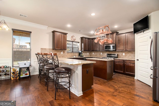 817 Nevis Way, Mcdonough, GA 30253 - kitchen with appliances with stainless steel finishes, a peninsula, a center island, dark brown cabinetry, and plenty of natural light