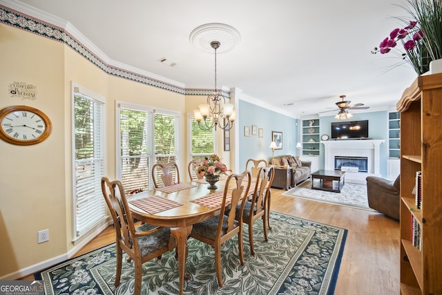 569 Fairway Dr, Woodstock, GA 30189 - dining room featuring ornamental molding, a chandelier, light wood-style flooring, a glass covered fireplace, and a ceiling fan