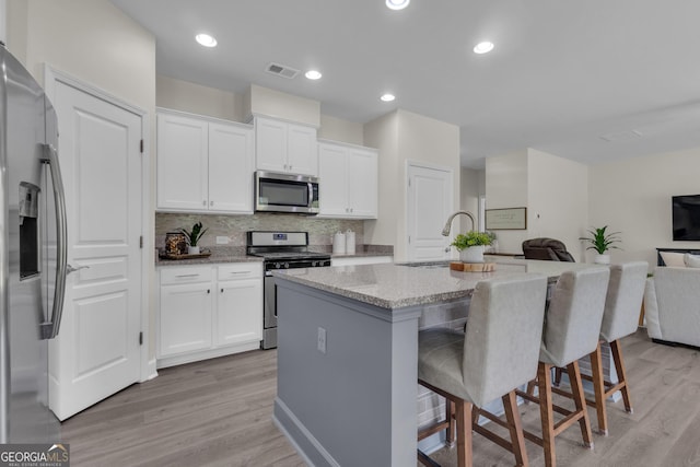 206 Roundwood Way, Peachtree City, GA 30269 - kitchen featuring appliances with stainless steel finishes, light stone countertops, open floor plan, white cabinetry, and light wood-style flooring