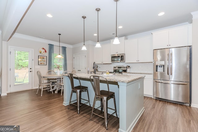 1243 Glenville Ct, Hoschton, GA 30548 - kitchen featuring appliances with stainless steel finishes, wood finished floors, a center island with sink, white cabinetry, and ornamental molding