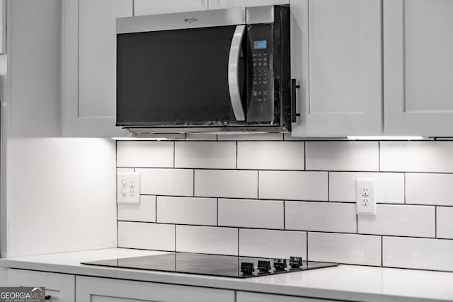 219 Fairview Dr, Morganton, GA 30560 - kitchen view of stainless steel microwave, black electric cooktop, tasteful backsplash, white cabinetry, and light countertops