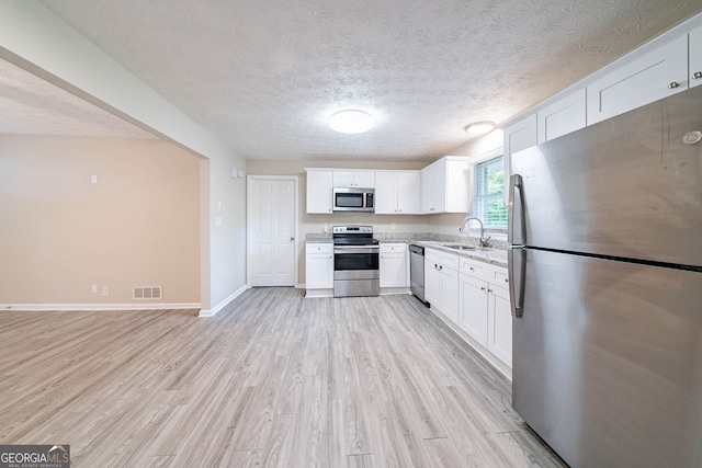 4457 Lincoln Jones Rd, Ellenwood, GA 30294 - kitchen with stainless steel appliances, light wood-style floors, a sink, white cabinets, and a textured ceiling