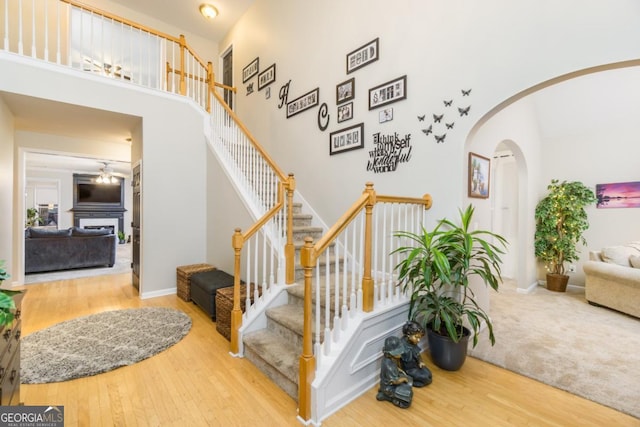 271 Double Gate Ct, Sugar Hill, GA 30518 - staircase featuring wood finished floors, a high ceiling, arched walkways, and a fireplace