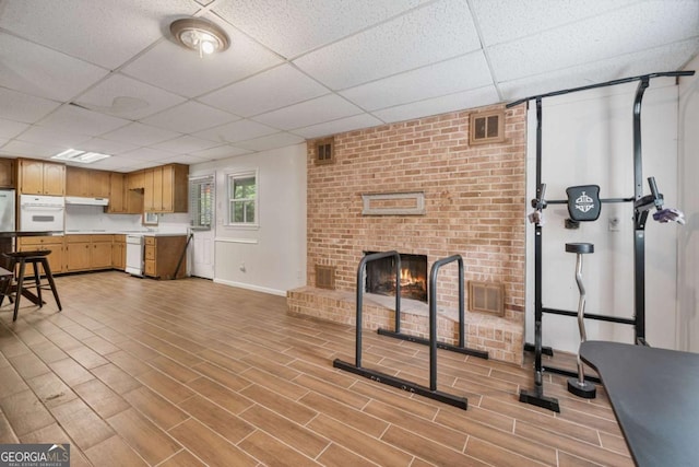 1777 E Gate Trl, Stone Mountain, GA 30087 - unfurnished living room featuring a drop ceiling, a brick fireplace, light wood-style flooring, and baseboards