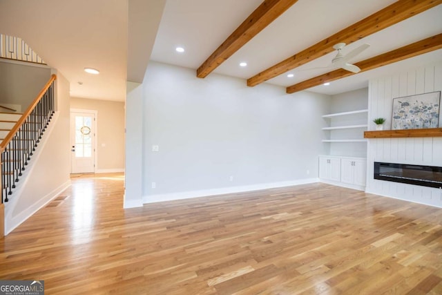 982 Wildberry Ct, Jefferson, GA 30549 - unfurnished living room featuring stairs, a glass covered fireplace, light wood-style flooring, a ceiling fan, and beamed ceiling