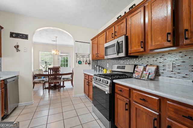 8180 Chapman Ter, Mcdonough, GA 30252 - kitchen with stainless steel appliances, brown cabinets, arched walkways, light tile patterned floors, and tasteful backsplash