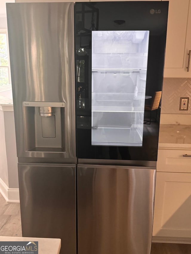 4867 Pinnacle Dr, Stone Mountain, GA 30088 - detailed view of stainless steel refrigerator with ice dispenser, tasteful backsplash, baseboards, light wood-style flooring, and white cabinetry