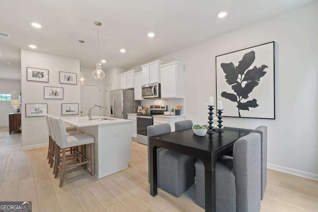 377 Navigator Ln, Mcdonough, GA 30253 - kitchen featuring stainless steel appliances, white cabinetry, a center island with sink, light wood-style flooring, and light countertops