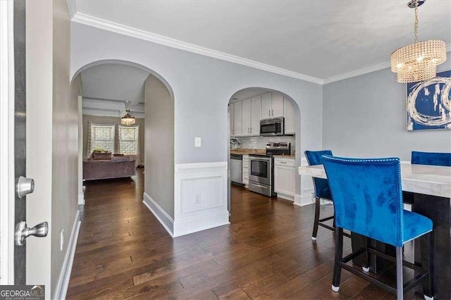 5880 Garden Cir, Douglasville, GA 30135 - dining room featuring dark wood finished floors, crown molding, a chandelier, arched walkways, and baseboards