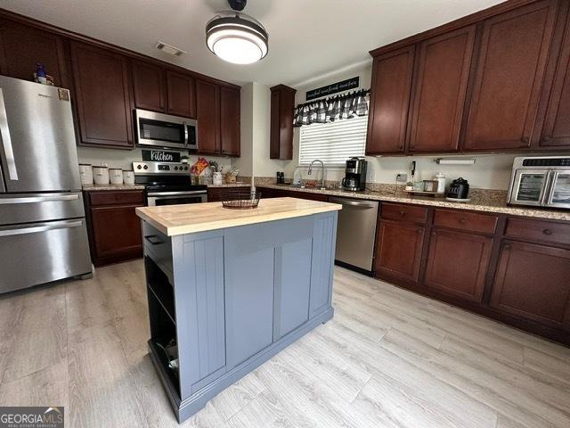 298 Timberwind Dr, Byron, GA 31008 - kitchen with appliances with stainless steel finishes, light wood-type flooring, a center island, dark brown cabinets, and a sink
