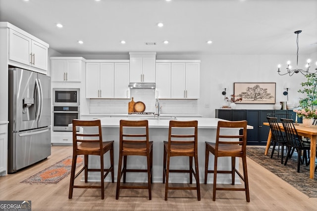 6045 Stargazer Way, Cumming, GA 30028 - kitchen with stainless steel appliances, light countertops, backsplash, light wood-type flooring, and a chandelier